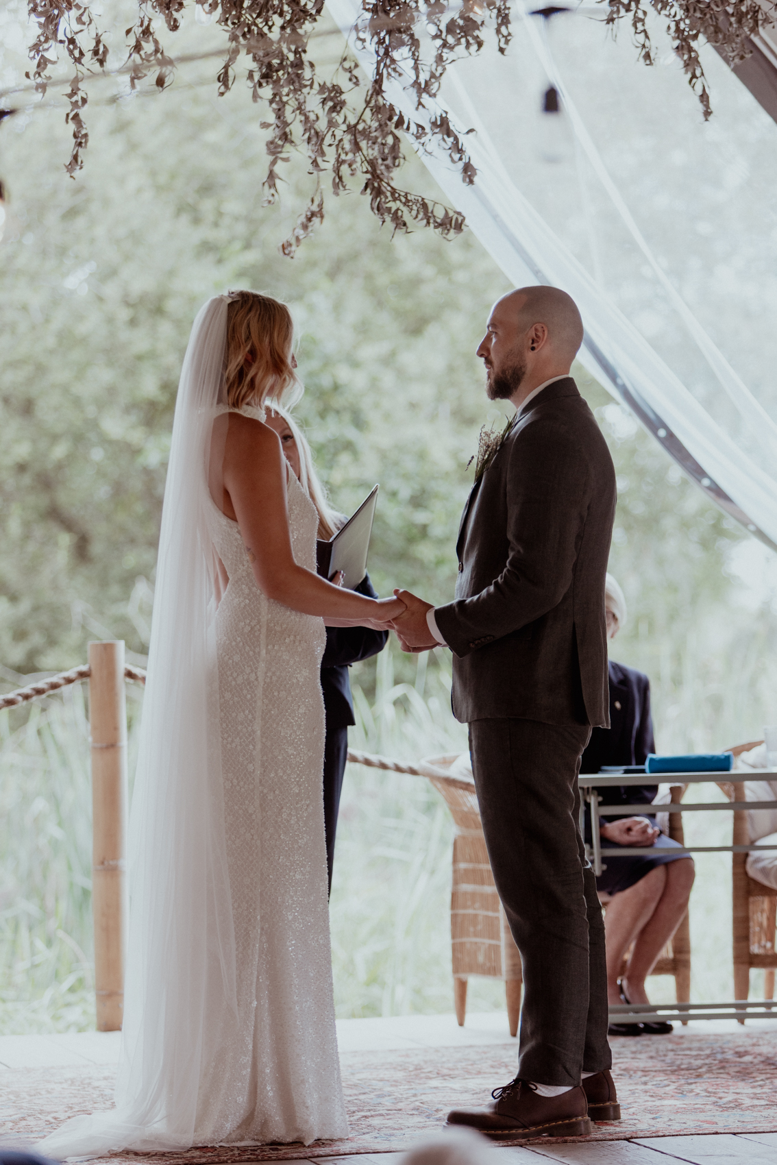 Bride and groom holding hands during their outdoor ceremony under a marquee
